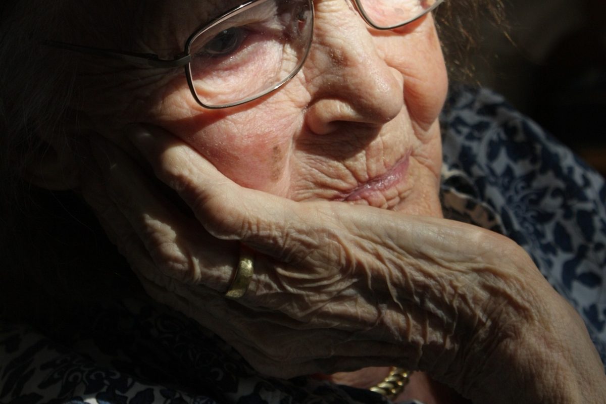 Eine alte Frau stützt ihr Gesicht in ihre Handfläche.