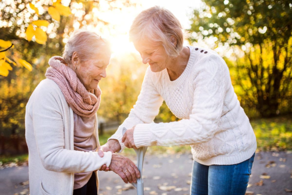 Eine Frau unterstützt eine ältere Frau beim Gehen mit einer Gehhilfe.