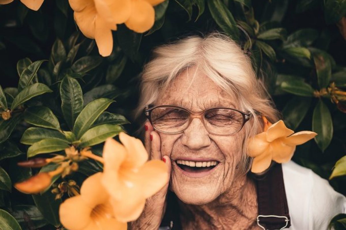 Eine Frau steht glücklich vor einem Busch mit Blüten